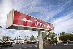 Red rectangular sign reading Drive Thru for fast food restaurant against blue sky and clouds