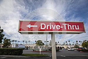 Red rectangular sign reading Drive Thru for fast food retaurant against blue sky and clouds