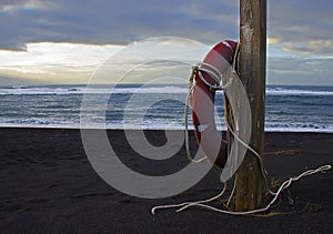 A red rescue circle to rescue people hangs on a wooden pole on the shores of the ocean