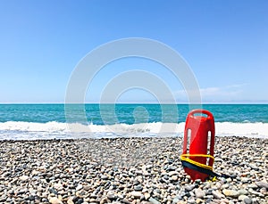 Red rescue float on rocky beach with sea panorama and no lifeguard