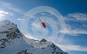 Red rescue helicopter flying over the view of the snowy rocks in Alpine ski resort