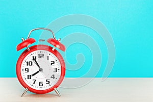 Red retro alarm clock with five minutes to eight o`clock, on wooden table on a blue background