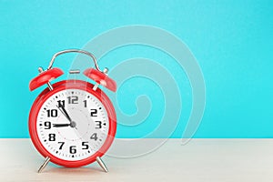 Red retro alarm clock with five minutes to nine o`clock, on wooden table on a blue background