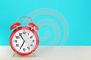 Red retro alarm clock with five minutes to seven o`clock, on wooden table on a blue background