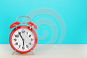Red retro alarm clock with five minutes to six o`clock, on wooden table on a blue background