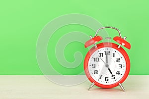 Red retro alarm clock with five o`clock, on wooden table on a green background