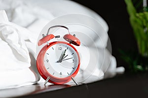 Red retro alarm clock near nightstand at bed with white blanket sheet at home in hotel bedroom. morning time to wake up early rise