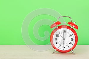 Red retro alarm clock with six o`clock, on wooden table on a green background