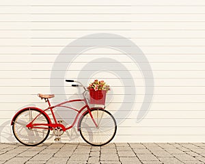 Red retro bicycle with basket and flowers in front of the white wall, background