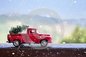 Red retro small car carrying christmas tree in the mountain in snowfall. Winter holiday concept.