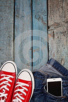 Red retro sneakers and smartphone in a jeans pocket on a blue wo