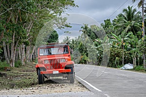 Red retro SUV car parked on the roadside of a tropical highway