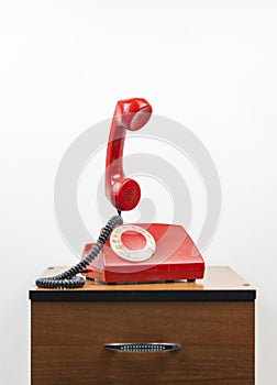 Red retro telephone on wooden nightstand