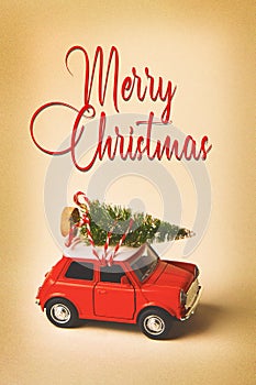 Red retro toy car carrying a Christmas tree on vintage background with text