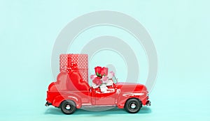 Red retro toy car delivering flower bouquet and gift box with hearts on turquoise background. Valentine day cute concept