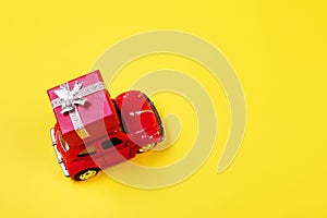 Red retro toy car with gift box on yellow background. Flowers, gifts  delivery concept.