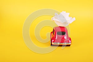 Red retro toy car with white rose flower on yellow background. Flowers, gifts delivery concept.