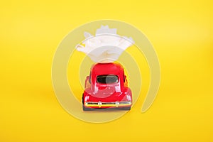 Red retro toy car with white rose flower on yellow background. Flowers, gifts delivery concept.