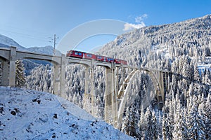 Red Rhaetian railway train on viaduct Langwies, sunshine, winter