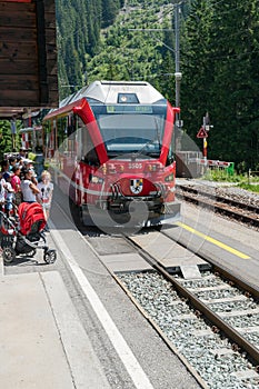 Red Rhatian railway train stops in Litzirueti to pick up passengers along the scenic Chur - Arosa line