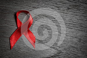 Red ribbon Aids awareness for World HIV/AIDS day on black and white wooden background