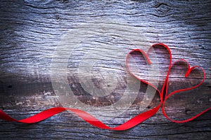 Red ribbon made heart shape on wooden background. Concept Valentine day. Love and happiness emotion.