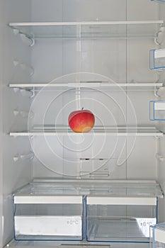 Red ripe apple on the shelf in the fridge. Health starvation, lose weight. Raw diet, starving concept. Vertical image