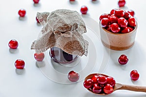 Red ripe cherries with jam jar and wooden spoon on white background. Flat lay. Food concept.