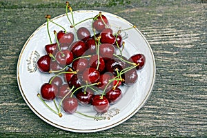 Red ripe cherries on a white plate on a wooden gray table