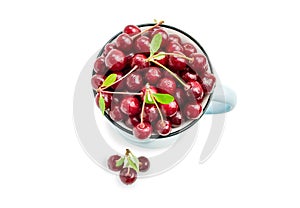 Red ripe cherry in a blue mug and three berries in front, top view. Sweet tasty fruits with water droplets in a cup isolated