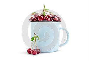 Red ripe cherry in a blue mug and three berries, front view. Sweet tasty fruits with water droplets in a cup isolated on white.