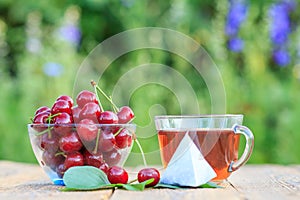 Red ripe cherry fruits with peduncles in glass bowl and cup of tea