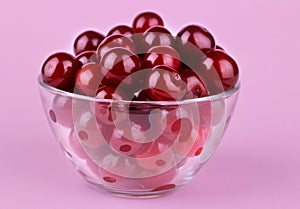 red, ripe, fresh cherries in a glass bowl on a bright pink paper background. close-up