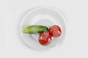 Red ripe juicy tomatoes and green cucumber on a white plate. The phallic image of natural components.