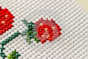 Red ripe strawberries embroidered with a cross-stich on a white canvas by hand. Close up, macro.