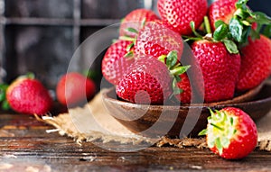 Red ripe strawberry in a wooden bowl on a rustic table, selective focus
