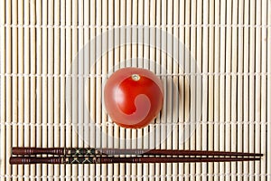 Red ripe tomato and chopsticks on bamboo mat closeup. Natural vegetables for dietary and healthy food. Chinese or japanese kitchen