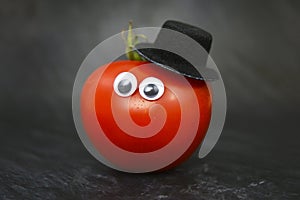 Red ripe tomato with funny goggle eyes and top hat on black background