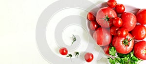 Red ripe tomatoes of different sizes with a sprig of parsley on a pink large plate on a white background. Healthy food concept