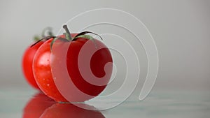 Red ripe tomatoes hit wet glass surface with splashes and rebound. Slow motion