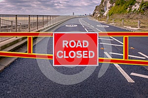 Red road closed barrier across an empty  tarmac road with white road markings and 30 mile per hour sign