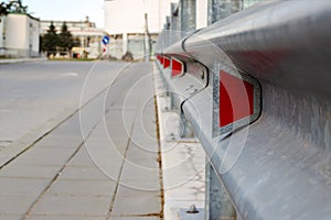 Red road reflectors along the road. Zinked or galvanized metal road fencing of barrier type, close-up. Road and traffic safety photo