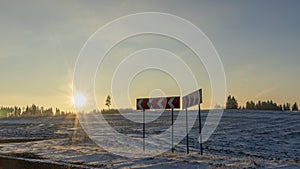 Red road sign for the direction of turning on the background of the countryside in wintertime at sunset. Field and road.