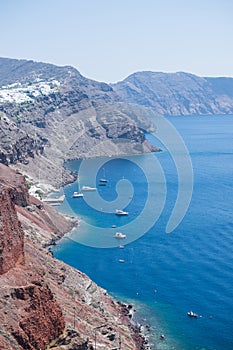 Red rocky coast of Santorini, Greece, with many boats in the blue sea