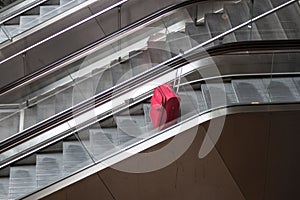 Red rolling suitcase on escalator traveling alone concept