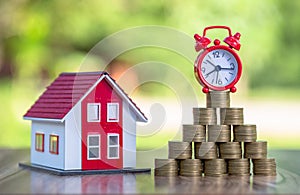 Red roof house And there are coins stacked with a red alarm clock placed on the pile of coins.Financial investment accounting