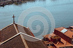 Red roofs with cross on river Douro background top view. Embankment with church roof and wooden cross in Porto, Portugal.