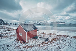 Red rorbu house shed on beach of fjord, Norway