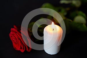 Red rose and burning candle over black background