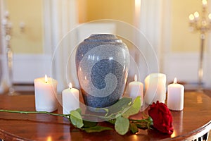 Red rose and cremation urn with burning candles